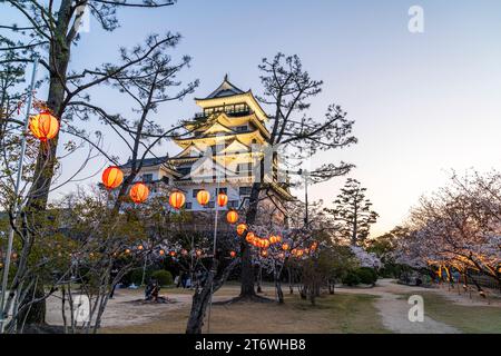 Schloss Fukuyama, Japan. Der beleuchtete weiße Donjon, umgeben von Kirschblüten mit Reihen beleuchteter Laternen, die im Frühling zwischen den Bäumen hängen. Stockfoto