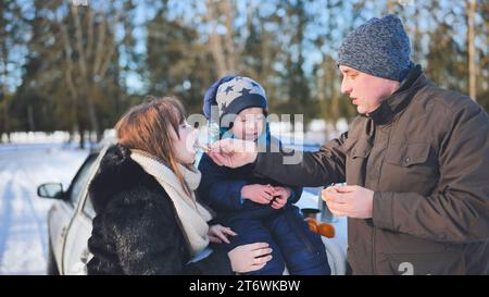 Eine junge Familie isst Mandarinen während eines Picknicks an einem Wintertag. Stockfoto