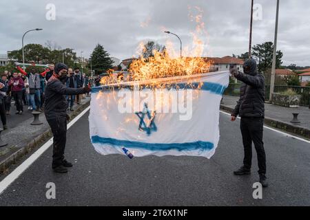 Zwei Menschen mit Kapuze haben eine Flagge Israels auf der Brücke zwischen Spanien und Frankreich verbrannt. Die Demonstration begann in Hendaye, Frankreich, und endete in Irun, Spanien. Die beiden Städte sind durch eine Brücke getrennt, die einen Fluss überquert, und dort fanden die Zwischenfälle mit der Polizei (auf französischer Seite) statt. Die beiden Grenzstädte sind durch einen Fluss getrennt. Stockfoto