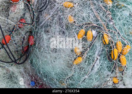 Rote und gelbe Bojen verstrickt in einem Stapel klarer Fischernetze auf einem Pier. Stockfoto