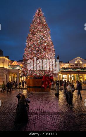 London, Großbritannien - 8. November 2023: Großer, geschmückter Weihnachtsbaum vor dem Covent Garden Market mit Leuten auf der Straße. Hochformat. Stockfoto