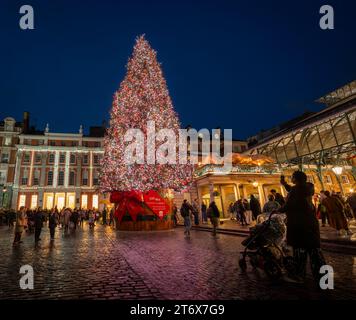 London, UK - 8. November 2023: Großer, geschmückter Weihnachtsbaum vor dem Covent Garden Market. Die Leute bewundern die Lichter auf dem Baum. Stockfoto