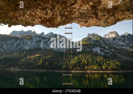 Wanderung um die beiden Gosauseen im oberösterreichischen Salzkammergut, am 29.10.2023. Das Bild zeigt einen Blick vom Wanderweg entlang des vorderen Gosuasees, auf das gegenüber liegende herbstlich bewaldete Seeufer mit dem Gebirgszug des Gosaukamms. Der Wanderweg wird vom über liegenden Steilhang überdacht. Der Weg ist auch in die Wand geschlagen. Von der Wand hängt eine Stahlleiter, die Kletterer für ihre Ausfflüge in die Wand benutzen. 2023 - Wanderung um die beiden Gosauseen im oberösterreichischen Salzkammergut, am 29.10.2023. *** Wandern Sie um die beiden Gosau-Seen im Oberösterreich Stockfoto