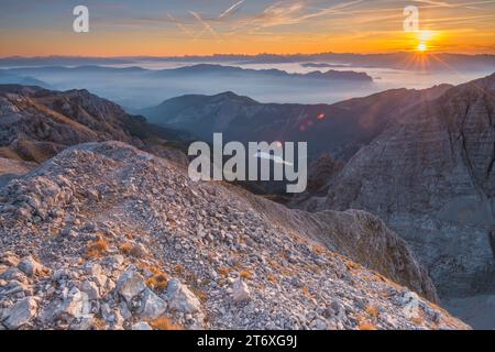 Das erste Sonnenlicht trifft auf die felsigen Berghänge mit dem See Tovel und den nebeligen Talböden. Hochalpiner Sonnenaufgang in den Brenta-Dolomiten. Stockfoto