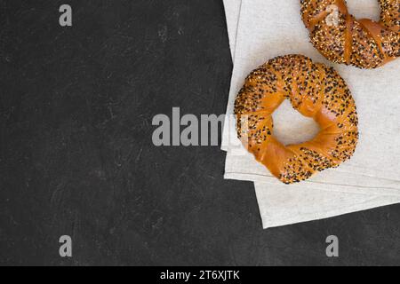 Leckerer knuspriger Bagel mit weißen und schwarzen Sesam auf Leinenserviette, dunkler Hintergrund. Frisches, köstliches Gebäck. Draufsicht, Kopierraum Stockfoto
