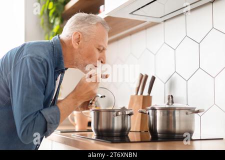 Senior Mann probiert Essen, während er auf dem Herd in der Küche kocht Stockfoto