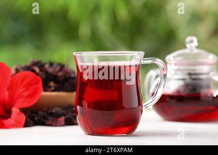 Glasbecher mit köstlichem Hibiskus-Tee auf weißem Holztisch draußen, Nahaufnahme Stockfoto