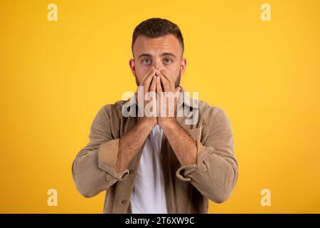 Ein schockierter junger kaukasischer Mann mit Bart in lässiger Weise bedeckt den Mund mit Händen Stockfoto