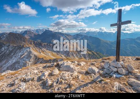 Bergkreuz, Gipfelkreuz auf der Spitze mit Blick auf die Bergketten in den italienischen Dolomiten. Herbstwandern auf einem scharfen Bergsteig. Stockfoto