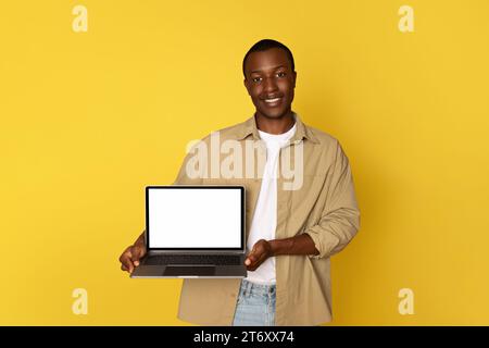 Ein lächelnder junger schwarzer Mann zeigt Laptop mit leerem Bildschirm für Arbeit, Studium, soziale Netzwerke Stockfoto