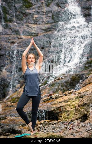 Fitte junge Frau, die Yoga in einer wunderschönen Landschaft mit Wasserfällen praktiziert. Konzepte von ganzheitlichem Erleben, Mensch und Naturverbund. Stockfoto