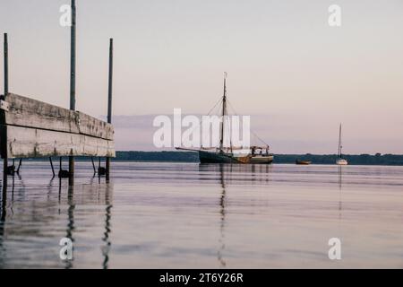 Altes Segelschiff neben einem Steg auf dem Wasser in der Dämmerung, Reflexion im Wasser Stockfoto