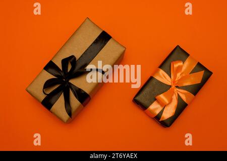 Zwei rechteckige Geschenkboxen, in Kraftpapier und schwarzem Papier gewickelt, verziert mit schwarzem und orangenem Satinband und Schleife, liegen auf orangem Hintergrund Stockfoto