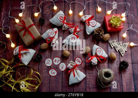 Flache Lagen. Adventskalender zu Weihnachten. Taschen mit Geschenken, Walnüssen, Konen, Soutache, Band, Kisten, Girlande, Zahlen, hölzerner Weihnachtsbaum sind aufgelegt Stockfoto