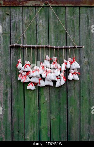 Der Adventskalender hängt an einer grünen Holzwand. Geschenktüten werden mit einem Soutache-Seil an einem Holzzweig befestigt Stockfoto