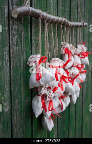 Der Adventskalender hängt an einer grünen Holzwand. Geschenktüten werden mit einem Soutache-Seil an einem Holzzweig befestigt. Nahaufnahme. Selektiver Fokus Stockfoto