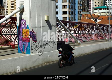 La Paz, Bolivien, 7. Juli 2022: Ein Motorradfahrer fährt an einem Wandgemälde auf einer Säule der Puente Gemelo/Zwillingsbrücke eines Faultieres vorbei, der gegen Chaqueos protestierte. Die Entwaldung ist insbesondere in Bolivien im letzten Jahrzehnt zu einem großen Problem geworden; 2022 wurde Bolivien von Global Forest Watch wegen Primärwaldverlusten an dritter Stelle der Welt gesetzt. Ein Großteil der Entwaldung ist die Politik der Regierung, die landwirtschaftliche Grenze des Landes auszuweiten, um Soja und Rinder für den Export nach China zu produzieren. Stockfoto