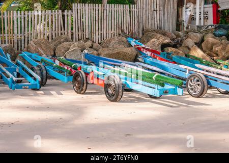 Viele farbenfrohe Jet-Ski-Anhänger aus Holz parken am Sandstrand in der Nähe großer Steine und Zäune. Lokal hergestellt in Thailand Stockfoto