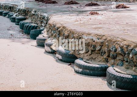 Alte Autoreifen, die als Verstärkung des Gehsteigs aus Beton verwendet wurden, gebaut am Sandstrand bei hohen Gezeiten, perspektivische Sicht Stockfoto