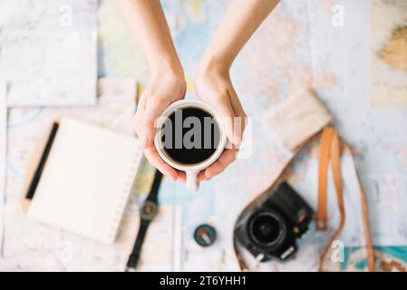 Draufsicht die Hand der Person, die eine Kaffeetasse hält, verschwommene Weltreisekarte Stockfoto