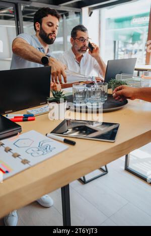 Männlicher Angestellter gießt Wasser in Gläser für seine Teamkollegen, während er im Büro arbeitet. Stockfoto