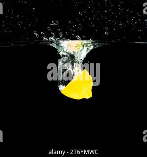 Reife halbe Zitrone, die in Wasser fällt, spritzt vor schwarzem Hintergrund Stockfoto