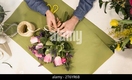 Erhöhte Aussicht männlicher Tourist, der Blumenstrauß mit grünem Schreibtisch bindet Stockfoto