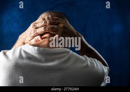 Mann, mit gedrehtem Rücken, verzweifelt, mit Händen auf dem Kopf vor blauem Hintergrund. Stockfoto