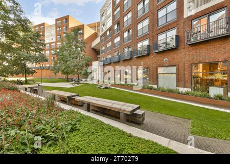 Ein städtischer Park mit Bänken und Pflanzen im Vordergrundbereich, umgeben von roten Backsteingebäuden auf beiden Seiten Stockfoto