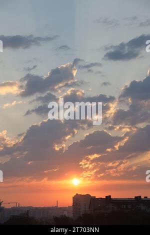 Wunderschöner Sonnenaufgang mit warmem orangenem Sonnenlicht und Sonnenstrahlen durch den bewölkten blauen Himmel Stockfoto
