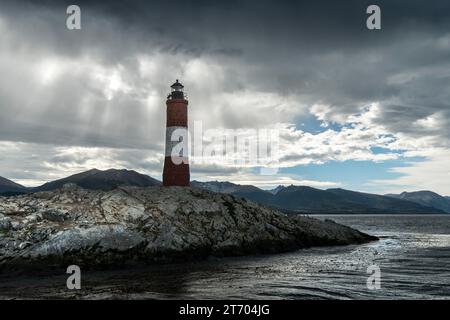 Panoramablick auf die felsige Insel, wo sich der Leuchtturm Les Eclaireurs befindet, unter einem bewölkten Himmel und die Berge im Hintergrund. Ushuaia, Ti Stockfoto