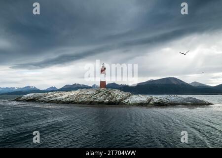 Panoramablick auf die felsige Insel, wo sich der Leuchtturm Les Eclaireurs befindet, unter einem bewölkten Himmel und die Berge im Hintergrund. Ushuaia, Ti Stockfoto