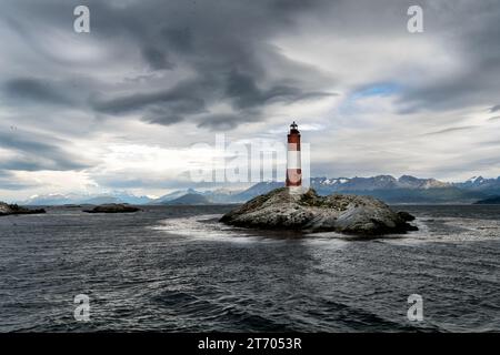 Panoramablick auf die felsige Insel, wo sich der Leuchtturm Les Eclaireurs befindet, unter einem bewölkten Himmel und die Berge im Hintergrund. Ushuaia, Ti Stockfoto