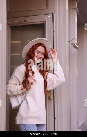 Lächelnde Frau mit Hut in der Nähe von Gebäuden im Freien Stockfoto