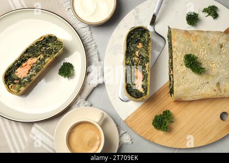 Köstlicher Strudel mit Lachs und Spinat serviert auf hellgrauem Tisch, flacher Lay Stockfoto