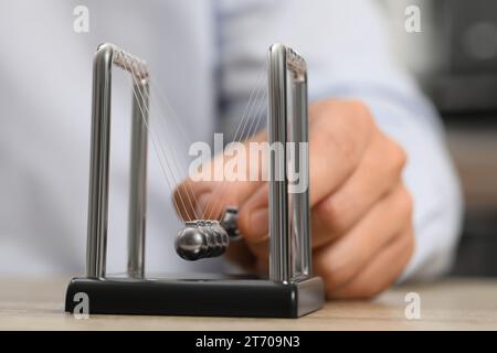 Mann, der mit Newtons Wiege am Tisch spielt, Nahaufnahme. Physikalisches Gesetz der Energieeinsparung Stockfoto