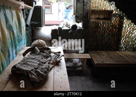 Ein Militärhelm eines ukrainischen Soldaten mit einer schweren kugelsicheren Weste auf einem Holztisch im Innenraum des Kontrollpunktes Stockfoto