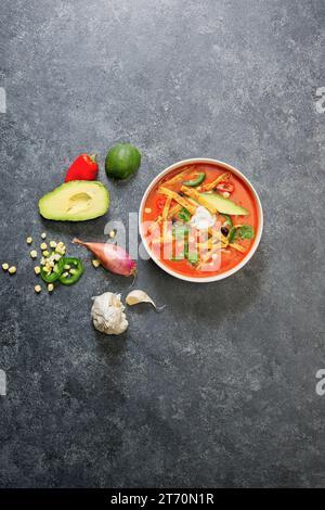 Hühnertortilla Suppe in Schüssel auf schwarzem Hintergrund mit Gemüse Stockfoto