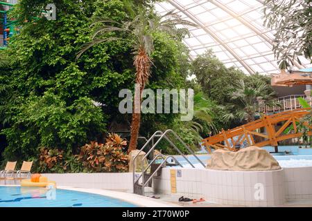 Innenraum des Aquaparks. Hydromassage im Erlebnispark mit grünen Palmen, Brücke und Schwimmbädern, Entspannungsbereich mit Wannen im Innenbereich Stockfoto