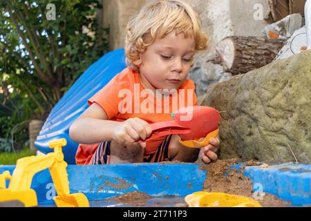 Ein kleiner Junge spielt im Sandkasten im Garten Stockfoto