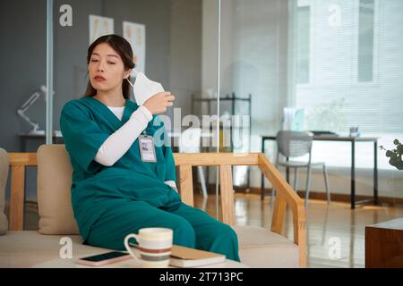 Erschöpfte Krankenschwester sitzt auf der Bank und nimmt die medizinische Maske ab Stockfoto
