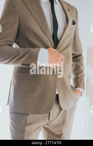Ein junger professioneller Mann, der einen stilvollen Anzug in einem modernen Innenraum mit einer weißen Wand trägt Stockfoto