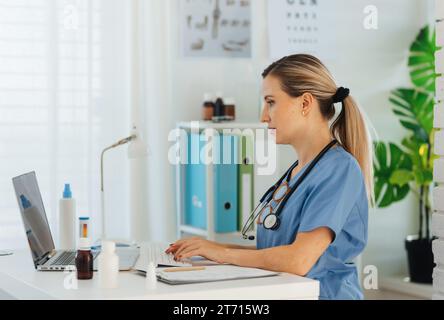Seitenansicht einer schönen Ärztin, die in der Arztpraxis am Laptop arbeitet. Arzt, der Papiere und Verwaltung macht. Stockfoto