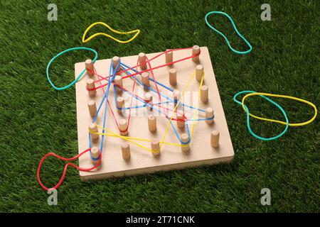 Holzgeoboard mit Gummibändern auf Kunstrasen. Lernspielzeug für die motorische Entwicklung Stockfoto