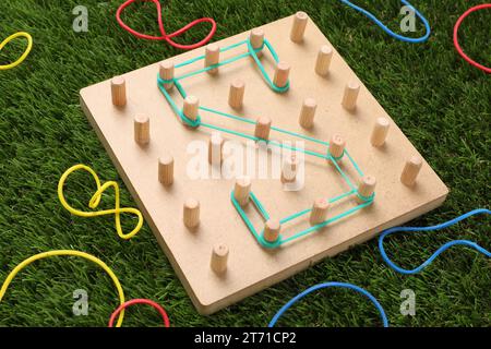 Geoboard aus Holz mit dem Buchstaben S aus Gummibändern auf Kunstrasen. Lernspielzeug für die motorische Entwicklung Stockfoto