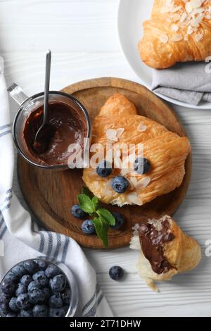 Köstliche Croissants mit Mandelflocken, Schokolade und Heidelbeeren serviert auf weißem Holztisch, flach gelegt Stockfoto