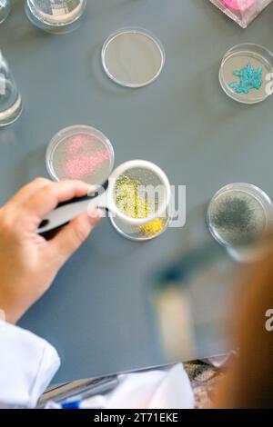Wissenschaftlerin untersucht goldene Glitzerprobe durch eine Lupe im pharmazeutischen Labor Stockfoto