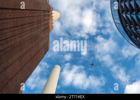 Zwischen Battersea-Kraftwerk und einem modernen Gebäude kann man ein Flugzeug sehen, das über die Hauptstadt fliegt. November 2023. Stockfoto