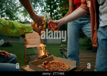 Freunde, die ein Picknick trinken, Bier trinken und Pizza essen, in der Nähe des Lagerfeuers Stockfoto