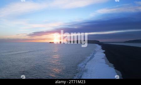 Schwarzer Sandstrand von Arctic reynisfjara in spektakulärer nordischer Landschaft mit Sonnenuntergang und Meereswellen, die an der Küste abstürzen. Blick aus der Vogelperspektive auf die isländische Küste und die natürliche Landschaft. Zeitlupe. Stockfoto